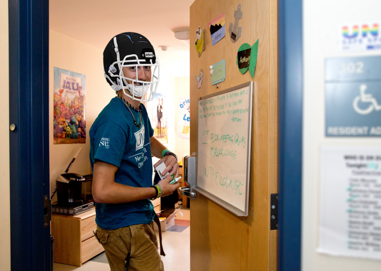 An RA in a dorm room wearing a football helmet