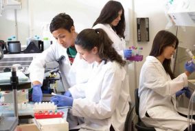 Four scientists wearing lab coats and gloves in a lab