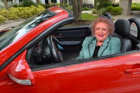 A very self-satisfied looking Betty White sitting in a red Ferrari.
