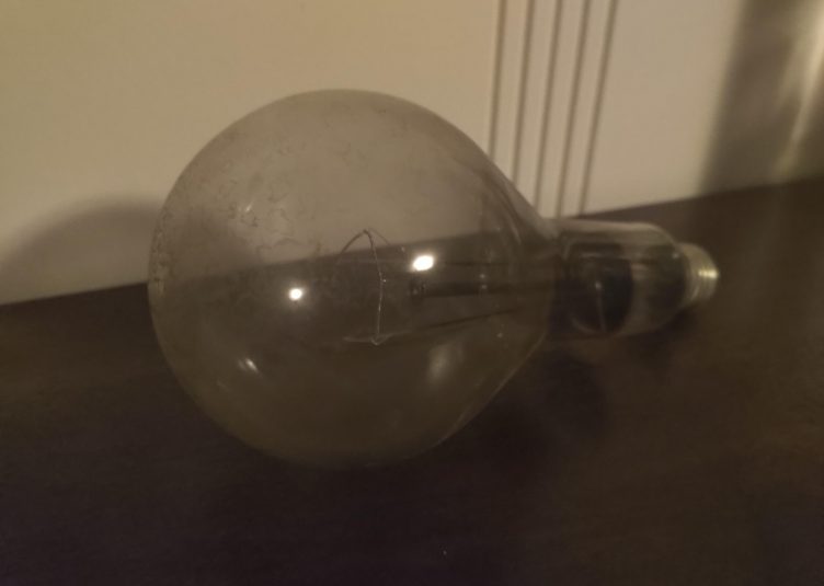 An old-looking lightbulb that has burned out, sitting on a table, collecting dust.