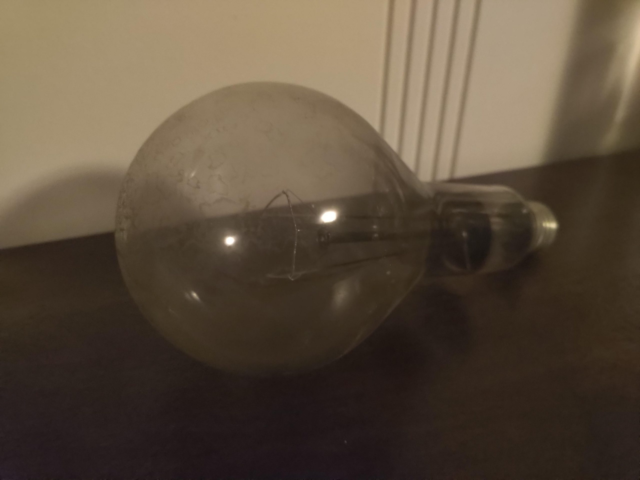 An old-looking lightbulb that has burned out, sitting on a table, collecting dust.
