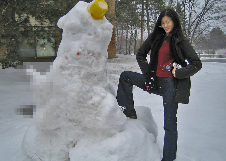 A large snowman with comically large and censored genitalia, and a woman proudly posing next to it.