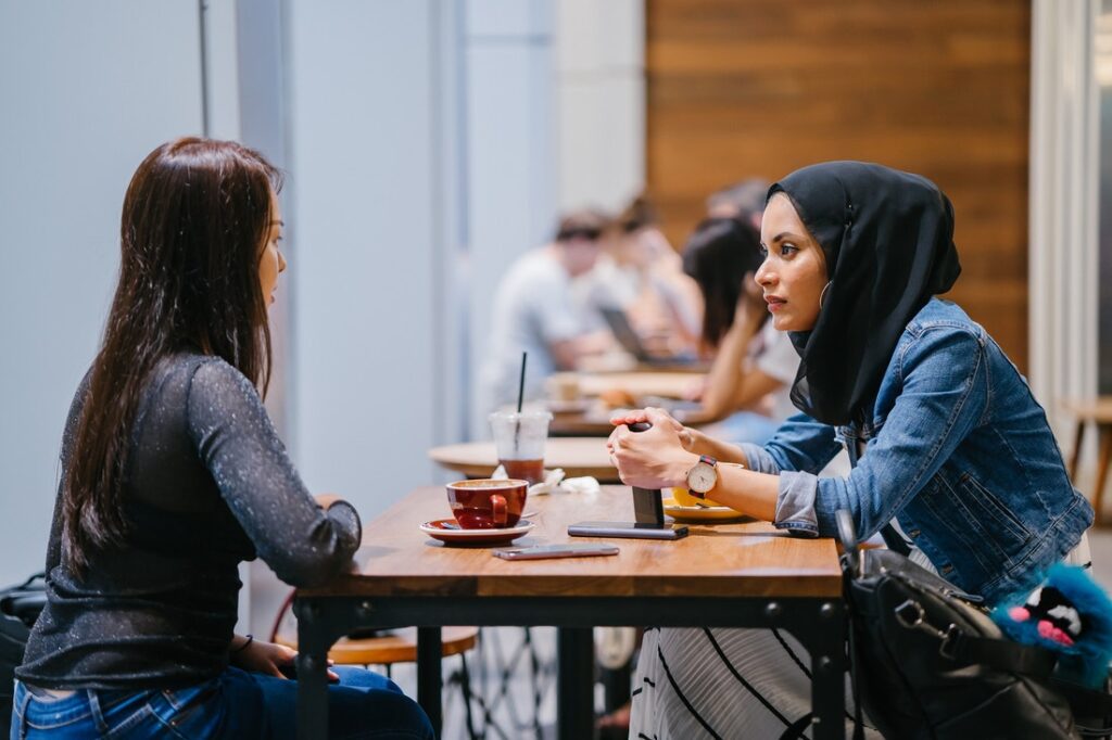 Two women have a conversation at a coffee shop.