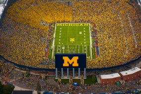 Overhead shot of a very filled Big House at night. Michigan logo is visible