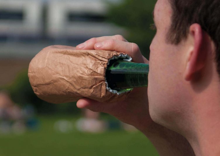 Man in a park drinking beer out of a paper bag.