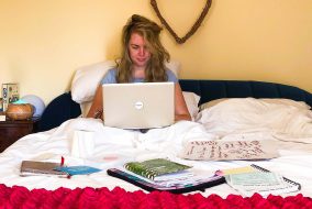Sickly, sad woman sitting in bed with laptop on lap