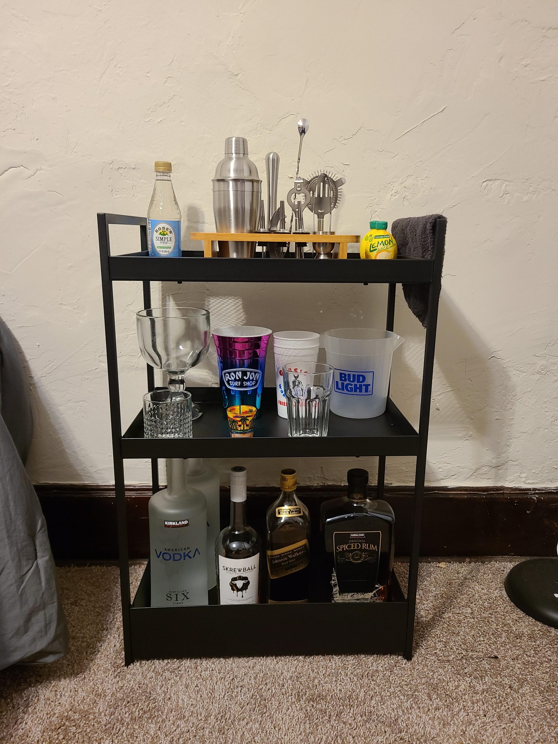 Black, metal bar cart with various liquors, glasses, and drink garnishes