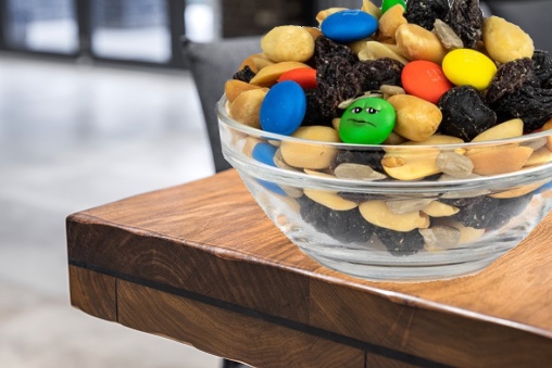 Bowl of M&M's on a table but one of them has a very distraught face.