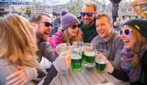 Smiling and laughing group of people doing cheers with glasses of green beer