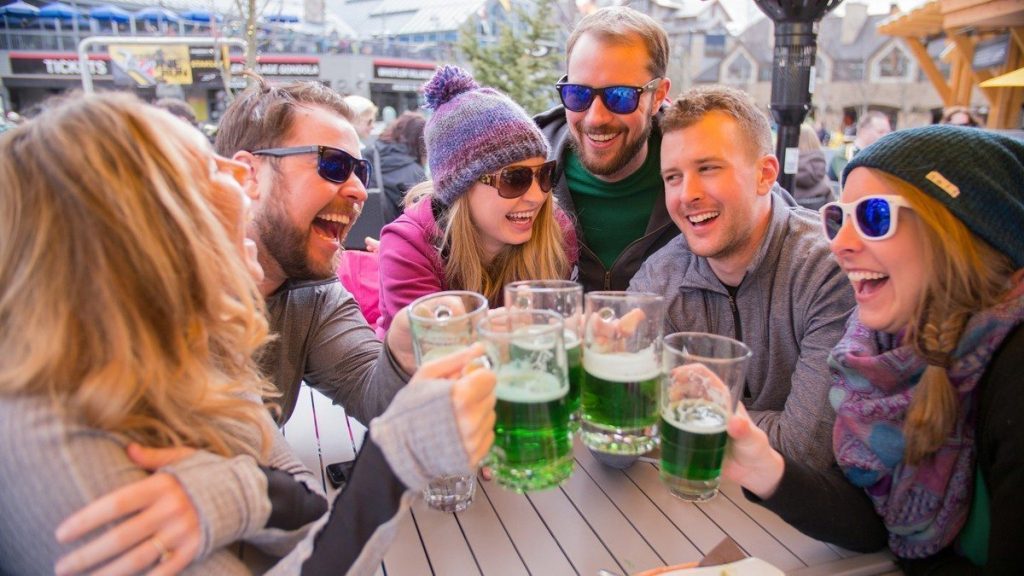 Smiling and laughing group of people doing cheers with glasses of green beer
