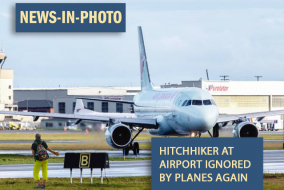 Picture of an airplane taxiing on the runway right past a person attempting to hittch a ride.