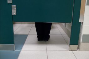 Legs underneath bathroom stall facing toilet