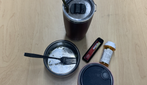 Cup, vape, prescription bottle, and empty food container with fork on table