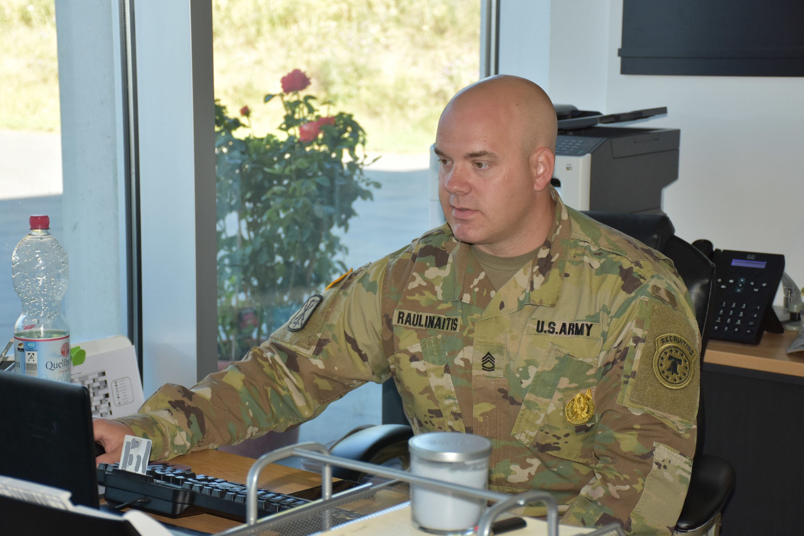 A man in an Army uniform sits, working at a computer.