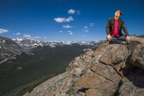 A man sits on the top of a large mountain range.