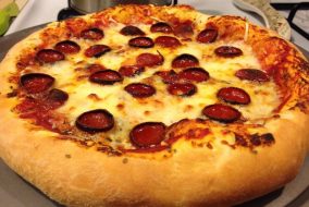 A thick-crusted pepperoni pizza sits on a baking sheet.