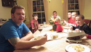 A man sits at a dining room table eating with kids of varying ages.