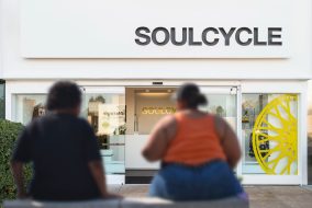 Two people sit outside a Soulcycle on a bench