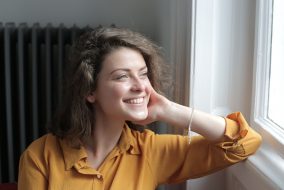white woman in yellow shirt stares happily out of window