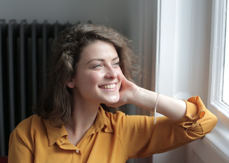 white woman in yellow shirt stares happily out of window