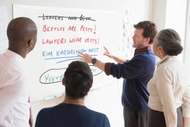People standing around a whiteboard with slogan ideas, such as "lawers wear vests," "beetles are pests," and "Kim Kardashian West."