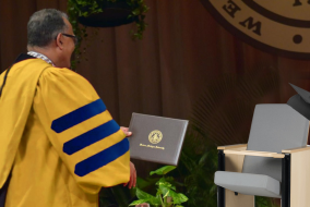 A university official awarding a Ph.D. to a lecture hall seat.