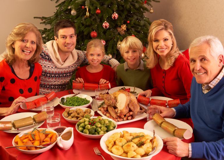 Large family sitting around a Christmas dinner, with decorations in the background.
