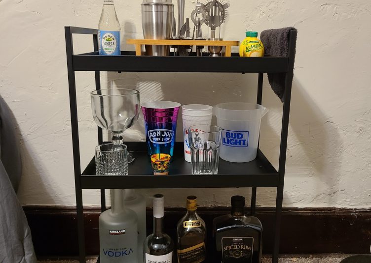 Black, metal bar cart with various liquors, glasses, and drink garnishes