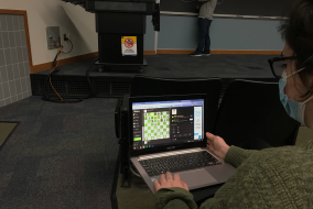 A student playing chess in the front row of a lecture.