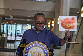 Chuck Schumer standing at podium holding photoshopped image of dentures