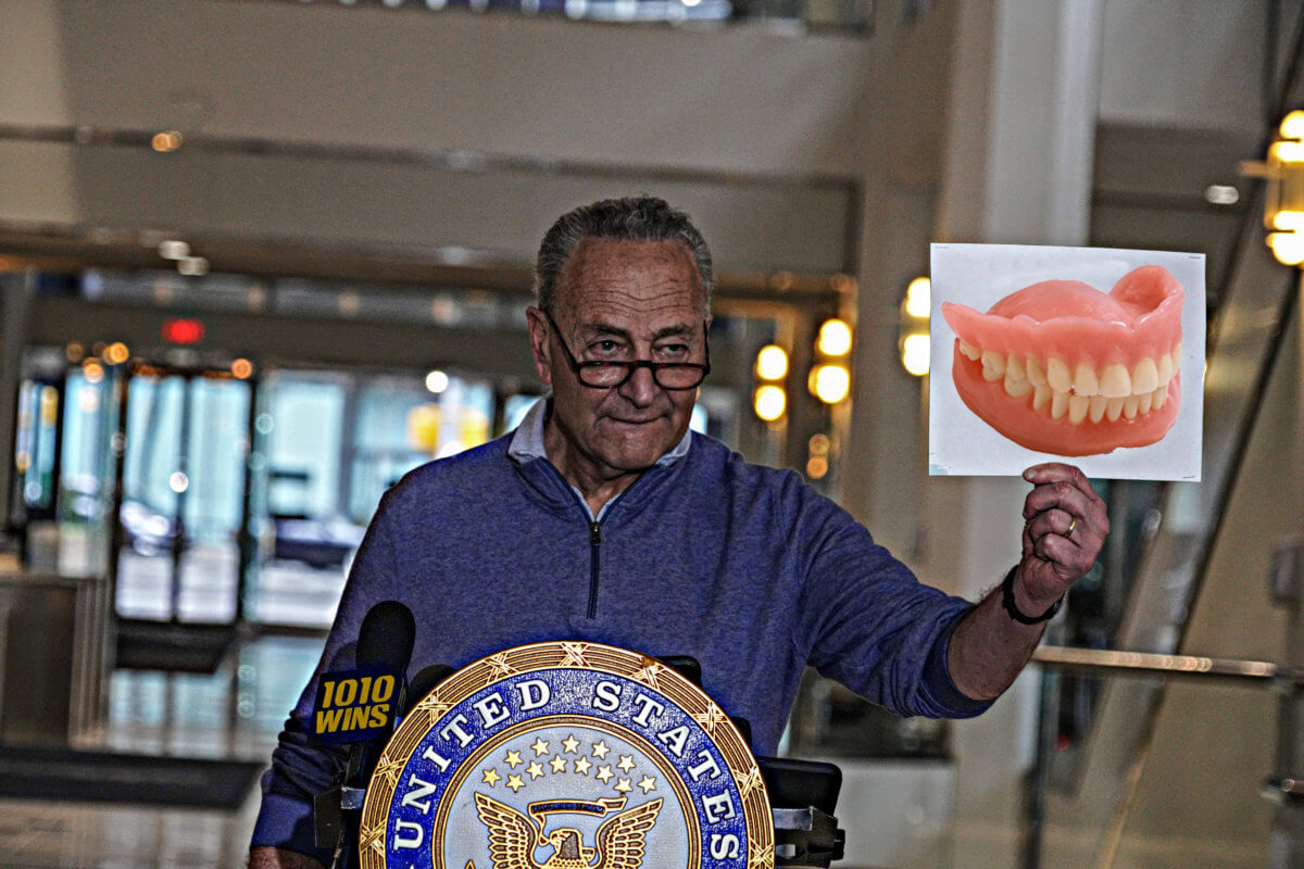 Chuck Schumer standing at podium holding photoshopped image of dentures