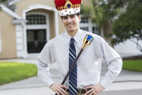 Landlord standing in front of his house wearing a crown and holding a scepter.