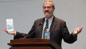 Mark Schlissel edited to holding container of Viagra while standing at podium