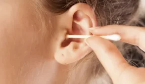 Close up picture of a person putting a q-tip in their ear.