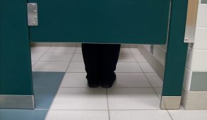 Legs underneath bathroom stall facing toilet