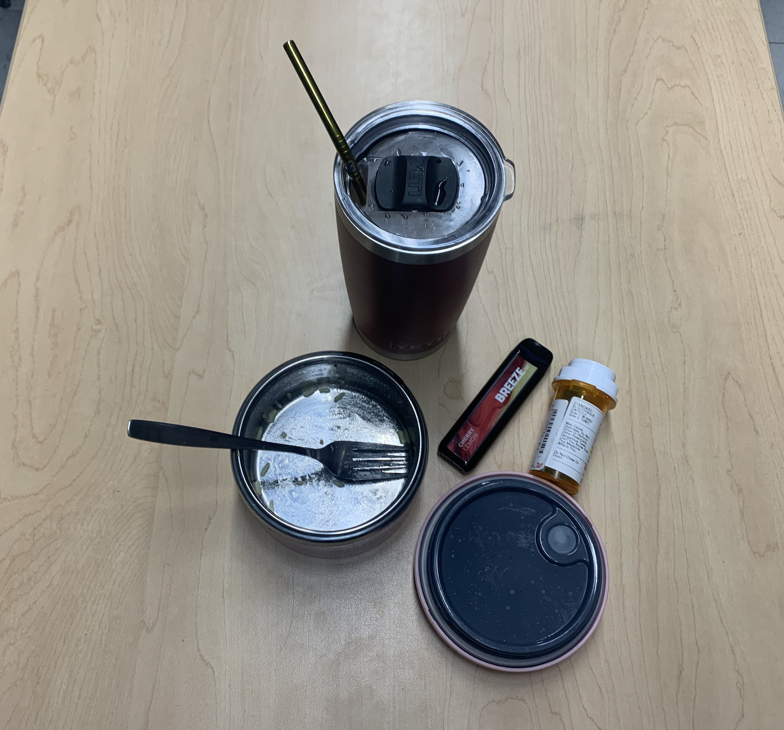 Cup, vape, prescription bottle, and empty food container with fork on table