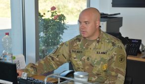 A man in an Army uniform sits, working at a computer.