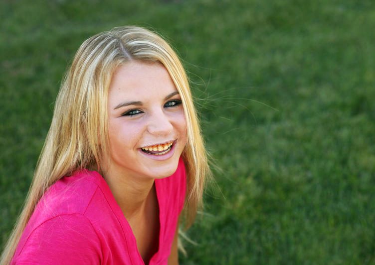 A blonde teen in a neon pink shirt smiles, showing yellowing teeth.
