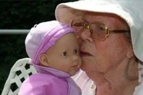 An older woman in a bucket hat presses her face to a baby doll.