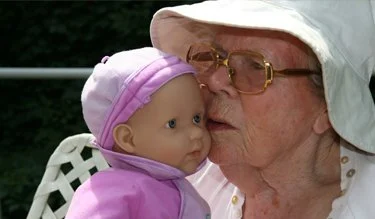 An older woman in a bucket hat presses her face to a baby doll.