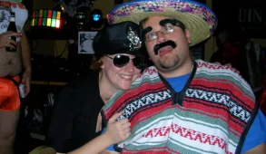 A man wearing a sombrero, fake eyebrows, and a fake mustache poses with a woman dressed as a police officer.
