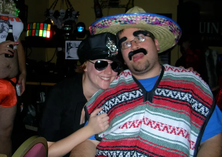 A man wearing a sombrero, fake eyebrows, and a fake mustache poses with a woman dressed as a police officer.