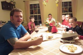 A man sits at a dining room table eating with kids of varying ages.