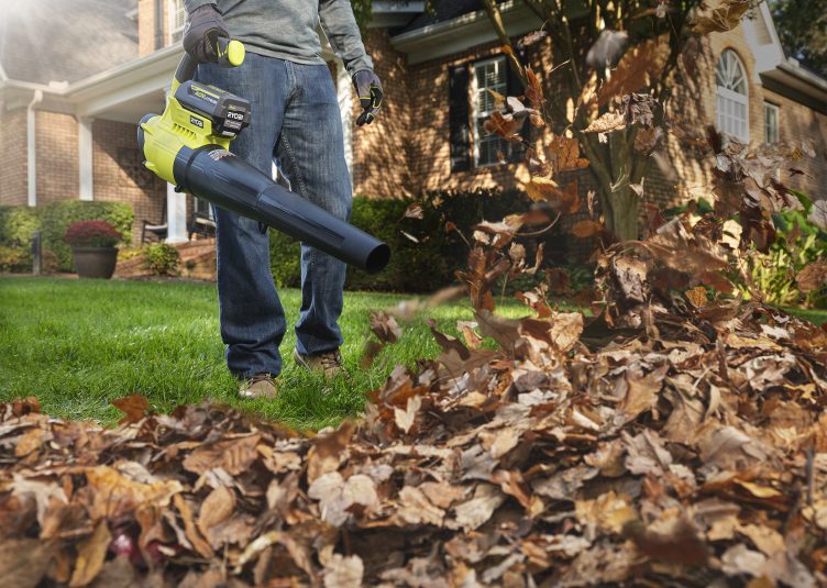 A man wearing jeans is seen from waist-down operating a leaf blower.