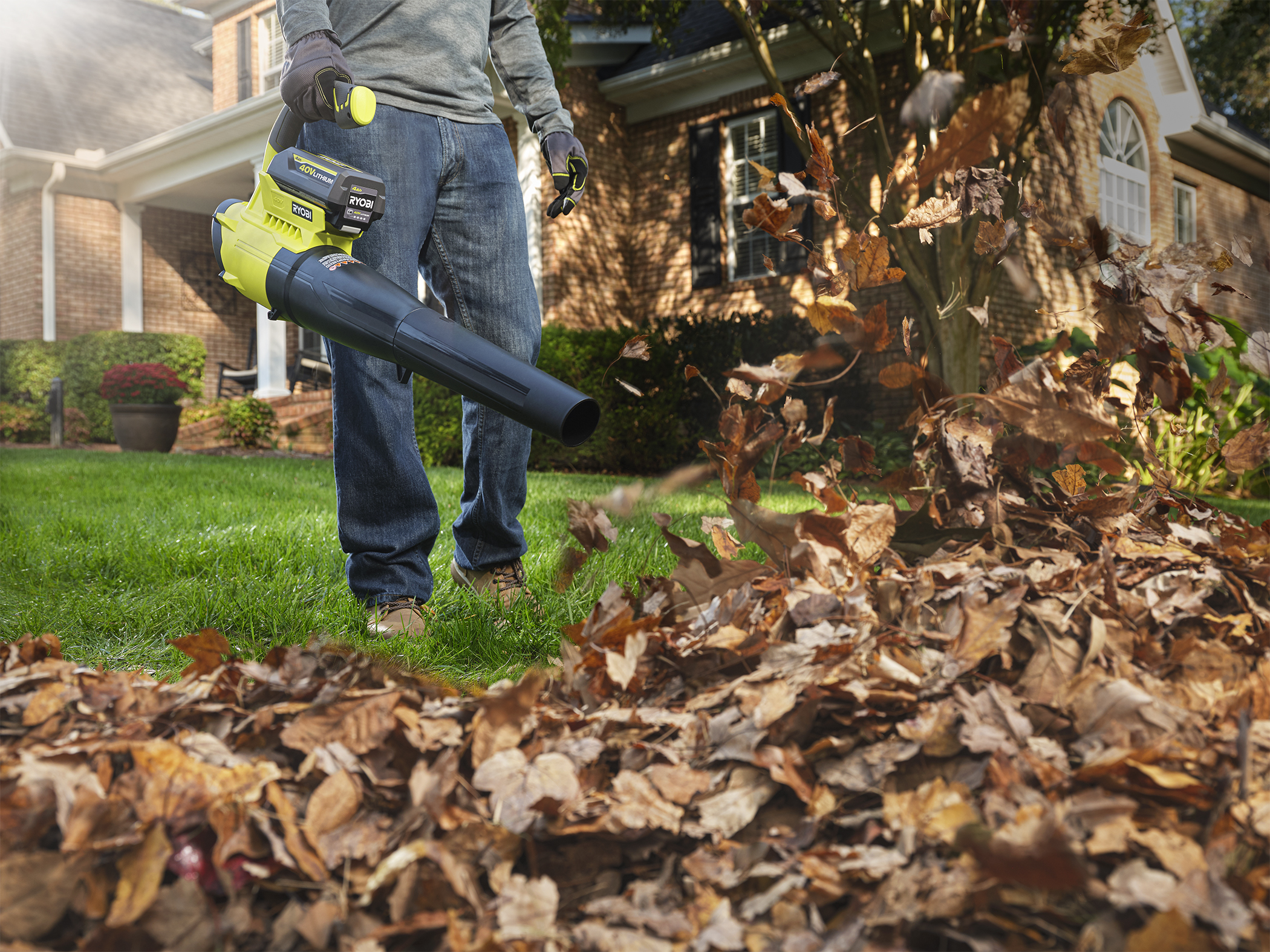A man wearing jeans is seen from waist-down operating a leaf blower.