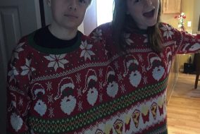 Siblings sharing a two-person Christmas sweater. One is a lot happier than the other.