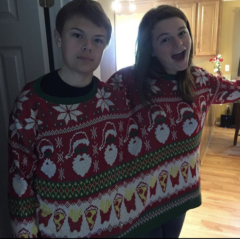 Siblings sharing a two-person Christmas sweater. One is a lot happier than the other.