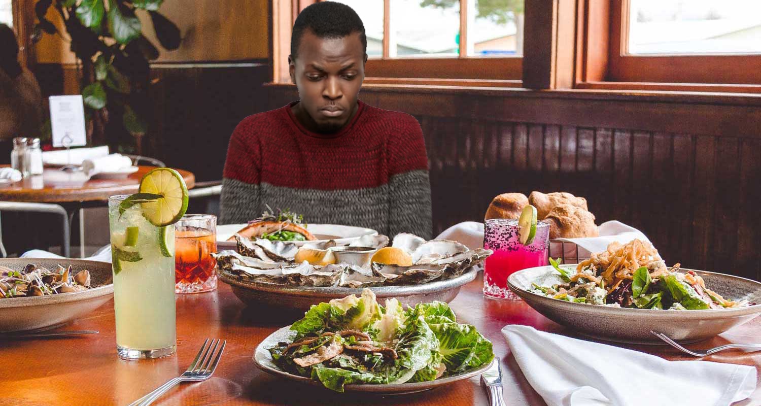 A man frowns at a restaurant table full of food.