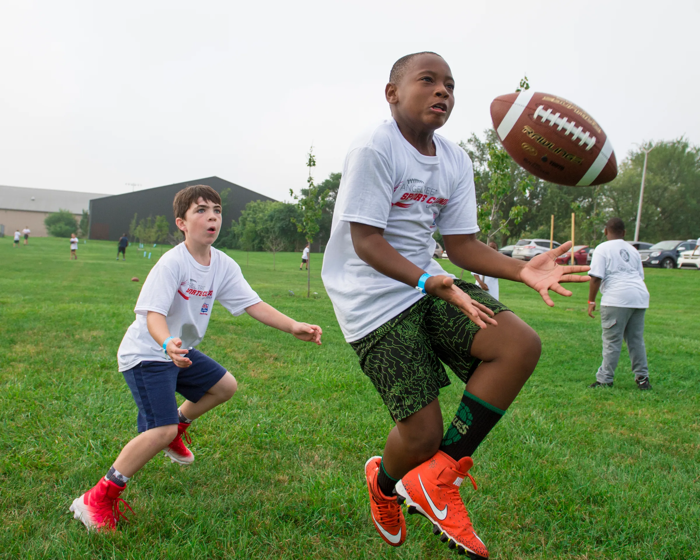 Two boys play football outside, one preparing to catch the ball.