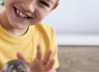 A boy wearing a yellow shirt holds a grey hamster.